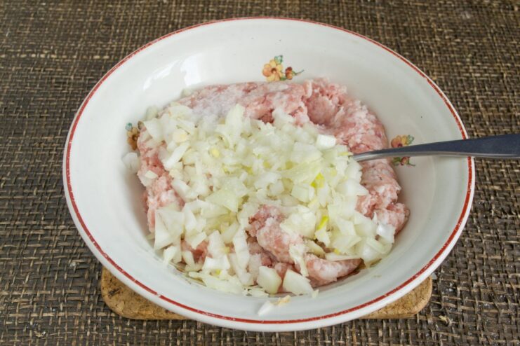 Preparing the savory meat filling for the potato dumplings A bowl of raw ground meat with chopped onions, salt, and pepper being mixed.