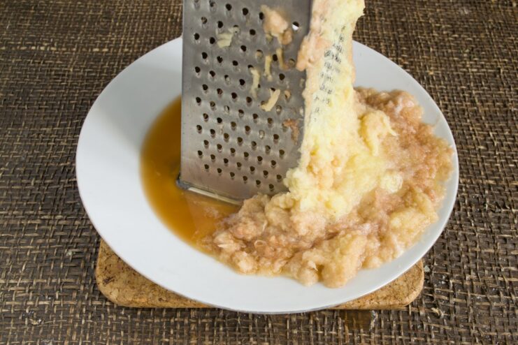 Grating potatoes finely to create a smooth dough A hand grating a raw potato on a fine metal grater.
