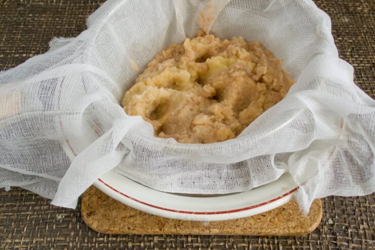 Squeezing out excess moisture from the potatoes is a key step Grated potatoes in a cheesecloth being squeezed to remove liquid.