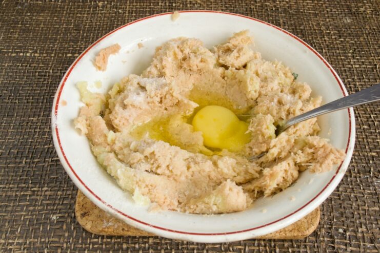 Binding the potato dough with an egg and salt An egg and salt being added to a bowl of squeezed grated potatoes.