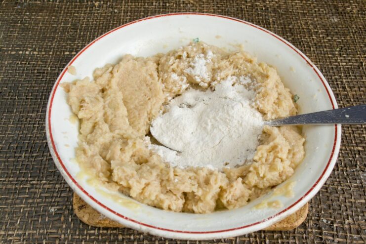 Mixing flour into the potato mixture to form the dough Flour being mixed into the potato and egg mixture in a bowl.