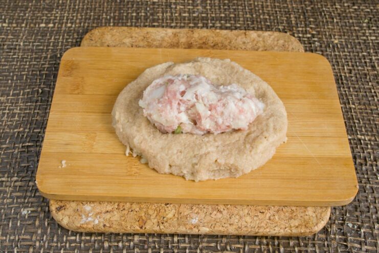 Assembling the dumplings: wrapping the meat filling in potato dough A small meat patty placed on a flat round piece of potato dough.