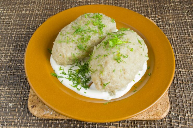 Serving the potato dumplings with a generous dollop of smetana and fresh dill Cooked potato dumplings in a bowl with smetana and garnished with fresh dill.