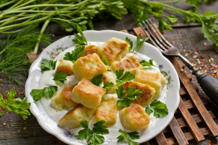 A plate of traditional Lithuanian Švilpikai potato dumplings, served with a creamy dill sauce and fresh herbs.