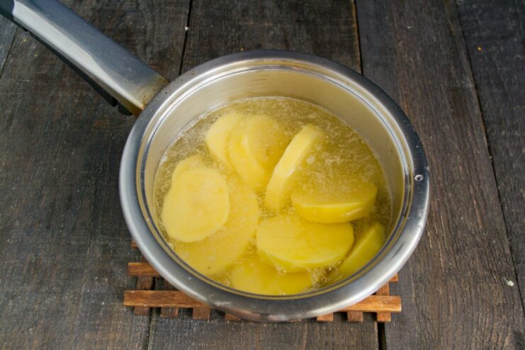 Boiling Potatoes and Garlic for the Švilpikai Dough Sliced potatoes and garlic cloves being added to a pot of boiling water to cook for the dumpling dough.