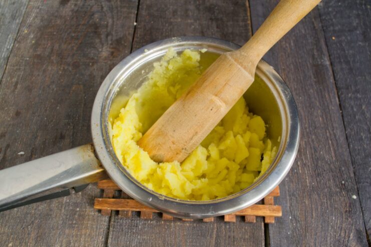 Mashing the Cooked Potatoes into a Smooth Puree Cooked potatoes being mashed with a potato masher in a pot to create a smooth base for the dumplings.