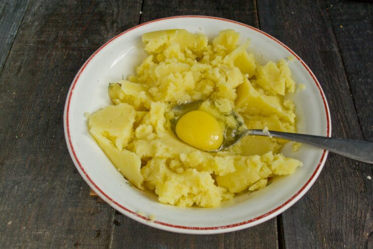 Combining Ingredients to Form the Potato Dough An egg, flour, and salt being added to the mashed potatoes in a pot to form the Švilpikai dough.