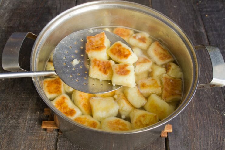 Quickly Boiling the Pan-Fried Dumplings to Finish Pan-fried Švilpikai dumplings being briefly boiled in a pot of water using a slotted spoon.