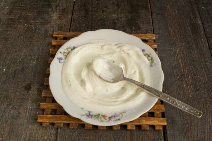 Preparing the Plate with a Creamy Dill Sauce A spoonful of creamy dill and smetana sauce being spread on a white plate as a base for the dumplings.