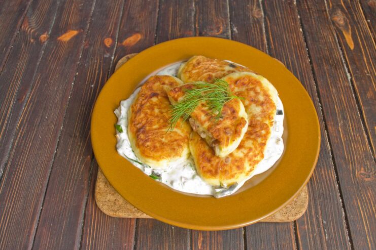 Serving the Potato Cutlets with a Dollop of Smetana Sauce A serving of hot potato cutlets with a side of creamy smetana sauce, garnished with dill.