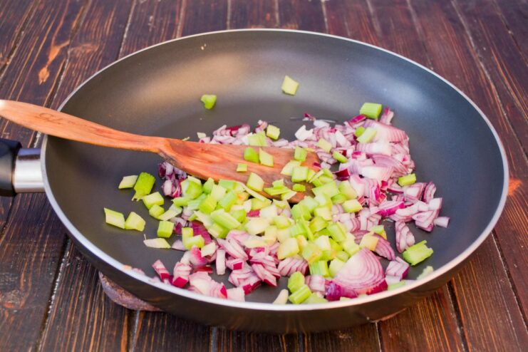 First step: Sautéing finely chopped red onion and celery in a pan. Chopped red onion and celery being sautéed in a hot frying pan.