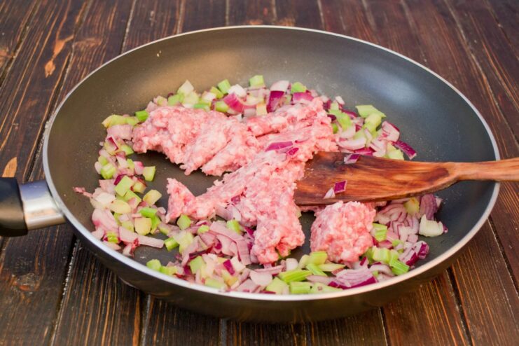 Cooking the minced meat filling for the potato pie. Minced meat being browned with onions and celery in a frying pan.