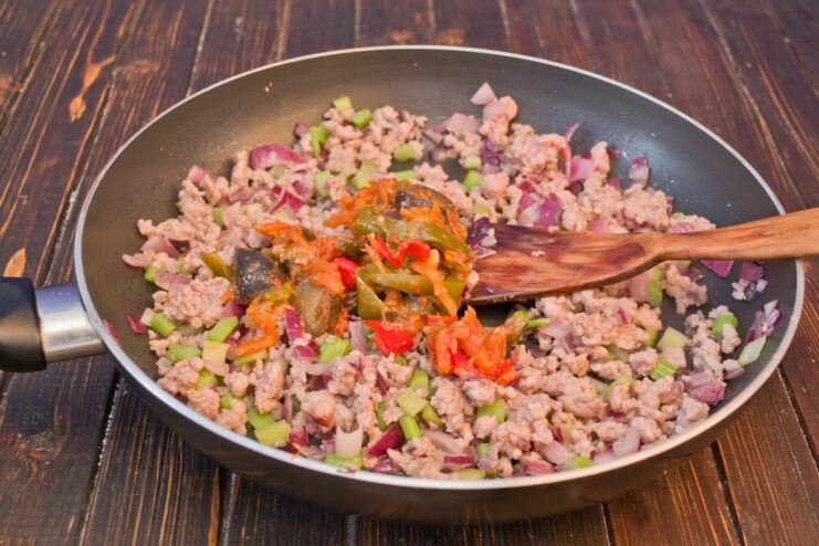 Adding vegetable stew to the minced meat for extra flavor. A spoonful of vegetable stew (salyanka) being added to the cooked minced meat in a pan.