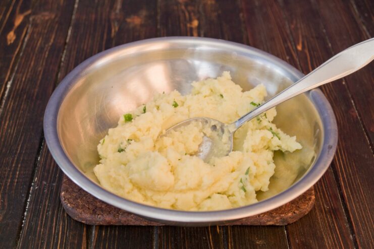 Preparing the creamy mashed potato topping with butter and green onions. A bowl of mashed potatoes with melted butter and chopped green onions being mixed.