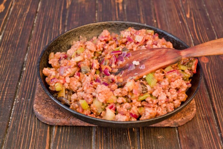 Assembling the pie: creating the bottom layer of savory minced meat. The cooked minced meat and vegetable mixture being spread evenly in a round baking dish.