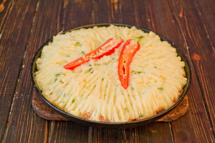 Creating the classic textured top on the potato pie with a fork. Mashed potatoes being spread over the meat filling in a baking dish, with fork marks on top.