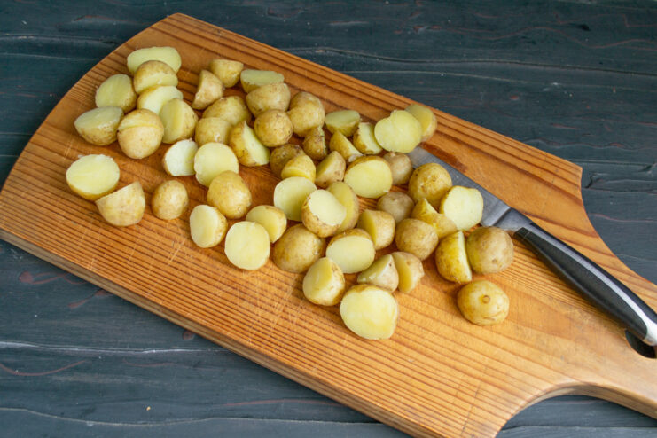 Preparing Potatoes for Frying A hand holding a knife, cutting a small boiled new potato in half on a cutting board.
