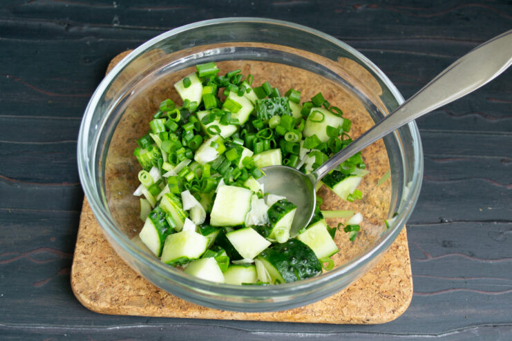 Adding Fresh Green Onions Finely chopped green onions being added to a bowl with cucumbers.