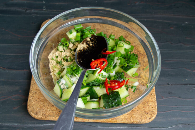 Seasoning the Salad with Soy Sauce Pouring soy sauce into a bowl of chopped cucumbers and green onions to make the dressing.