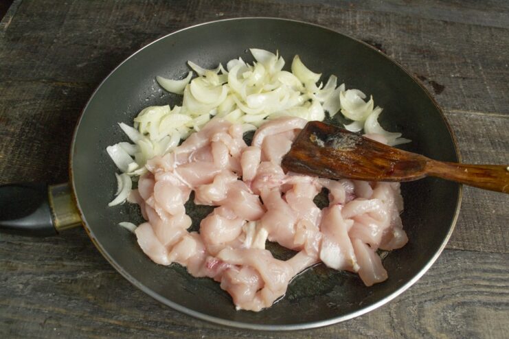 Step 3: Adding sliced chicken to the pan with onions. Sliced chicken breast being fried in a pan with sautéed onions.
