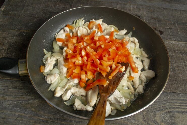 Step 4: Mixing in chopped bell peppers with the chicken. Diced red bell pepper added to the skillet with chicken and onions.