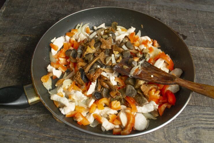 Step 5: Cooking mushrooms with the chicken and vegetables. Chopped mushrooms being cooked in a pan with chicken, onions, and peppers.