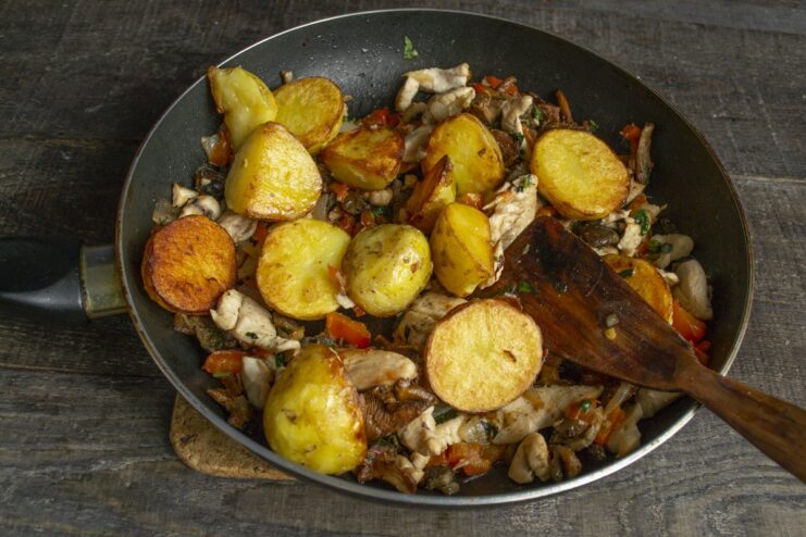 Step 8: Combining the fried potatoes with the chicken mixture. Golden fried potatoes being added to the skillet with the chicken, mushroom, and pepper mix.