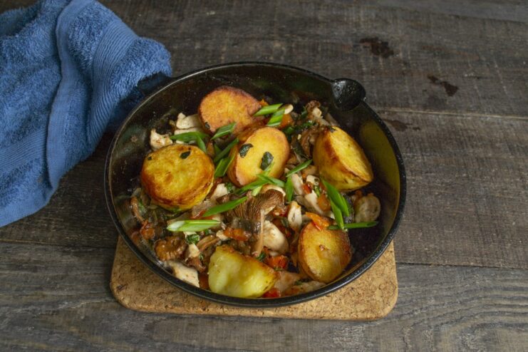 Final step: Serving the dish garnished with green onions. The final dish of potatoes with mushrooms and chicken in a serving skillet, garnished with chopped green onions.