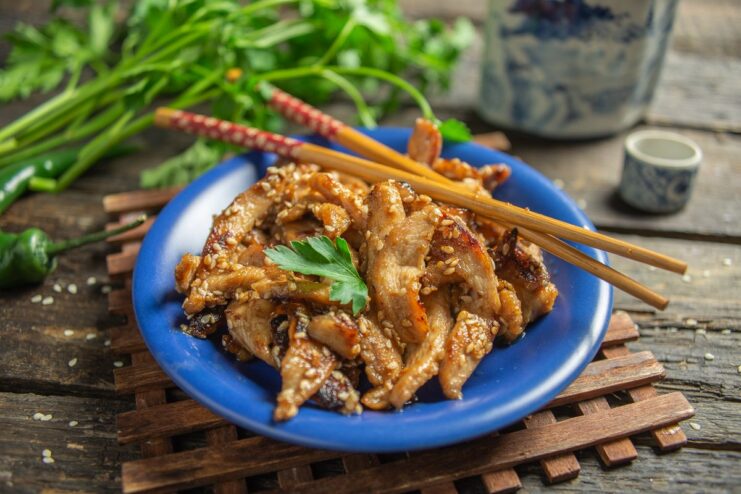 A plate of sweet and sour teriyaki chicken with sesame seeds, garnished with fresh herbs.