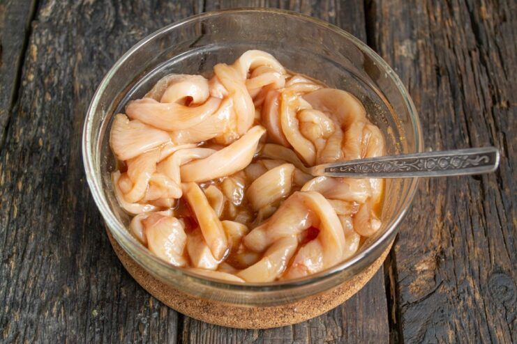 Sliced chicken marinating in a glass bowl of teriyaki sauce.