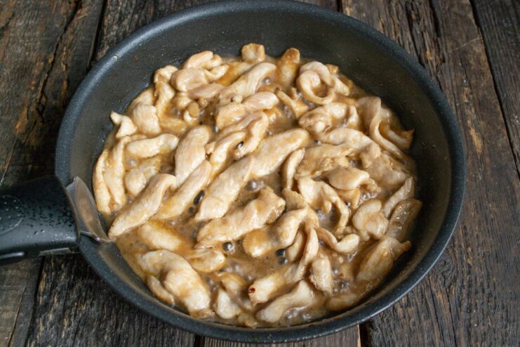 Marinated chicken strips being added to a hot pan with oil.