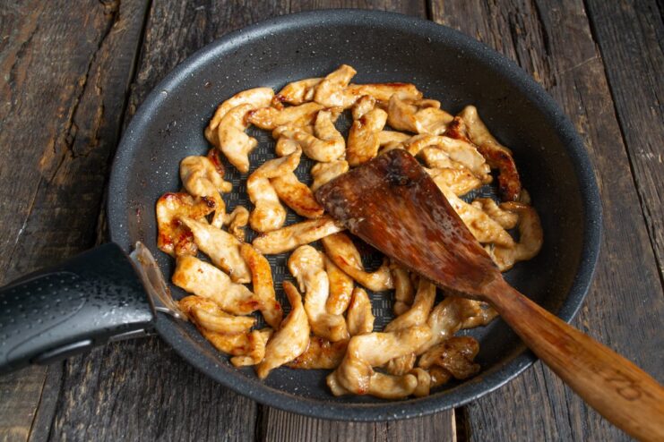 Chicken strips being stir-fried in a pan over high heat.