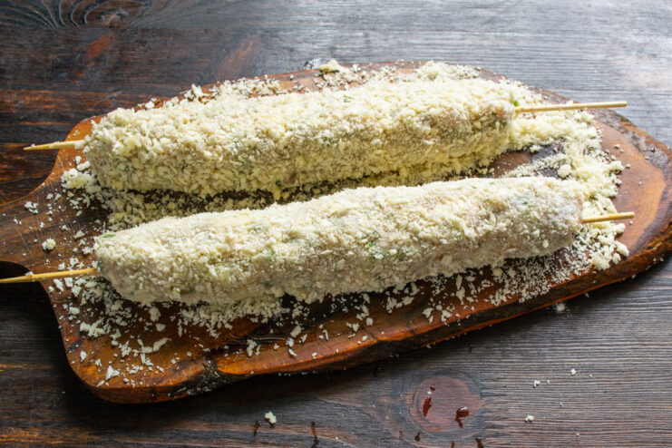 Final Breading Step: Coating with Breadcrumbs An egg-washed sausage on a skewer being generously coated with panko breadcrumbs.