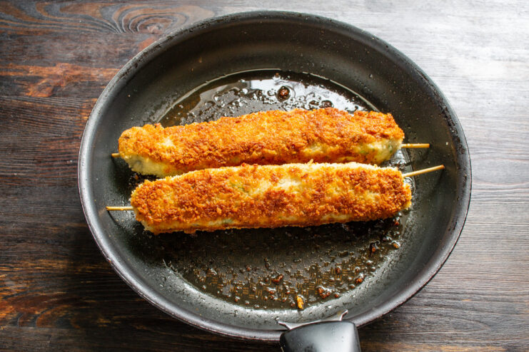 Ensuring the Sausages are Cooked Through Golden-brown sausages on skewers cooking in a pan, covered partially to steam and cook through.