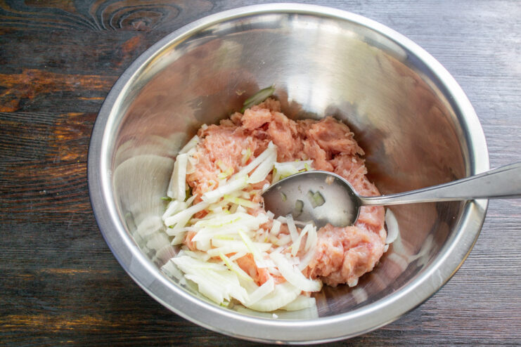 Adding Flavor with Diced Onion Finely diced onion being added to the ground meat mixture in a bowl.