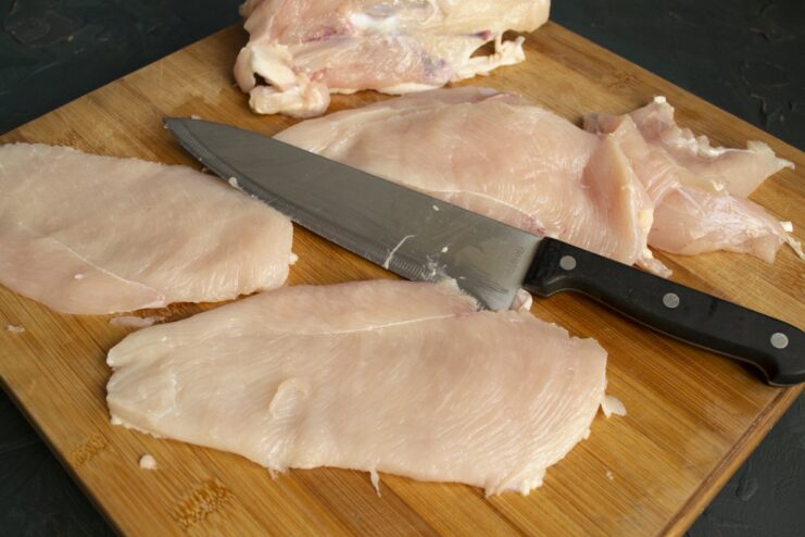 Slicing the chicken fillet to create thinner cutlets for pounding A chicken fillet being sliced in half horizontally to create two thinner pieces.