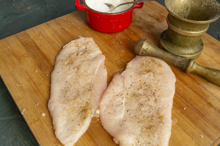Seasoning the pounded chicken fillets before chilling Pounded chicken fillets in a bowl, seasoned with salt and pepper.