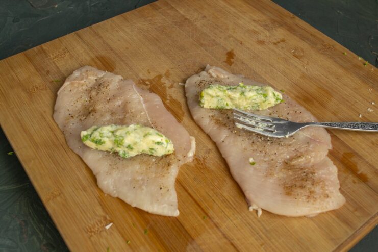 Step 4: Carefully rolling the chicken around the filling, sealing the edges A hand rolling a chicken fillet around a cylinder of herbed butter filling.