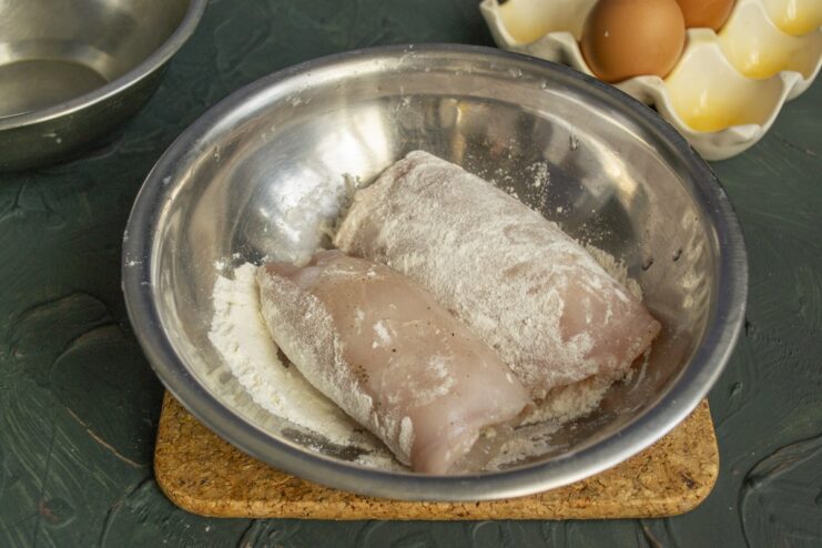 Step 4: Coating the chicken roll in flour to help the egg wash stick A rolled chicken cutlet being dredged in a bowl of white flour.