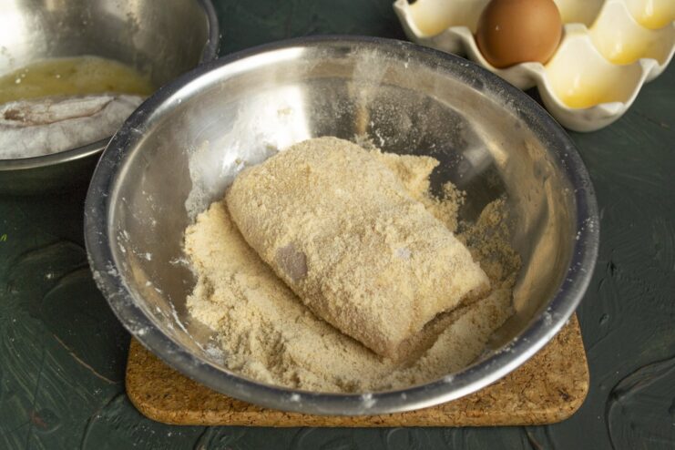 Step 6: Generously coating the cutlet in breadcrumbs for a crispy crust An egg-washed chicken cutlet being coated in a bowl of breadcrumbs.