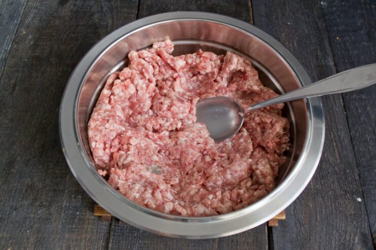 A bowl of ground meat with spices, salt, and water being added to it.