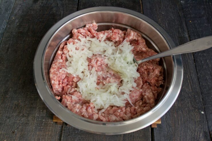 Chopped onion being added to a bowl of seasoned ground meat.