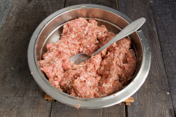 Hands mixing ground meat, onion, and spices in a glass bowl.