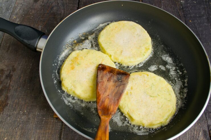 Potato flatbreads being fried to a golden-brown color in a pan.