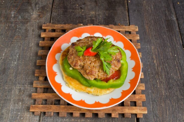 The final dish: a kotleta placed on a potato flatbread with bell pepper, garnished with parsley and chili.