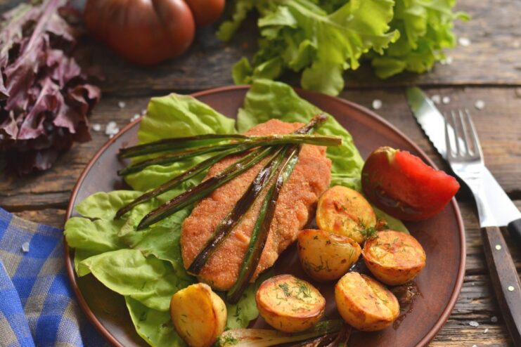 A plate of ready-to-eat Ground Chicken Kiev, garnished with greens and served with potatoes.
