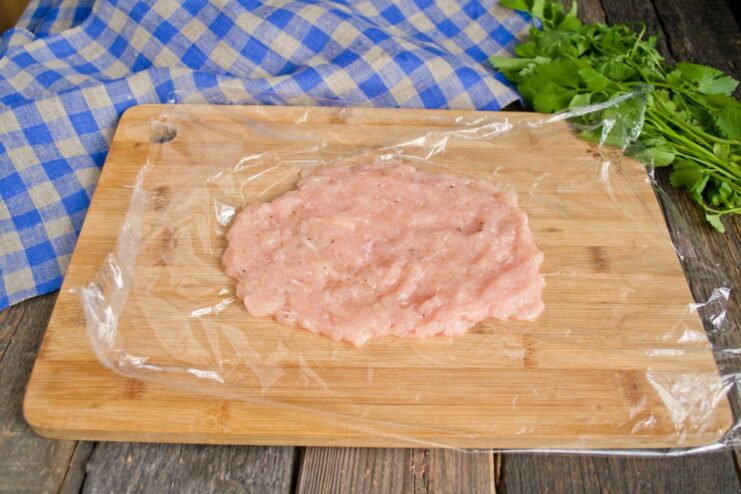Using Plastic Wrap to Easily Shape Chicken Kiev Patties A hand shaping a ground chicken patty on a piece of plastic wrap.