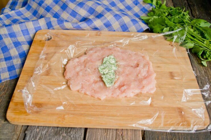 Adding the Herbed Butter Filling to the Chicken Patty A cylinder of herbed butter being placed in the center of a raw ground chicken patty.