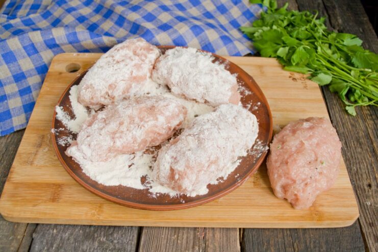 First Step of Breading: Coating Chicken Kiev in Flour Raw Chicken Kiev cutlets being coated in a plate of all-purpose flour.