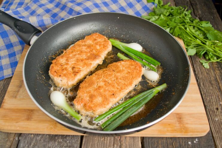 Frying Chicken Kiev to a Perfect Golden Brown Golden-brown Chicken Kiev cutlets frying in a pan with green onions.